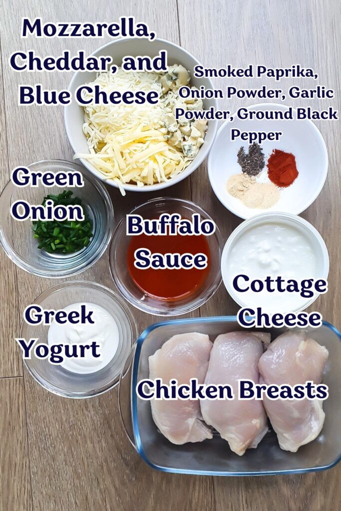 Ingredients for slow cooker buffalo chicken dip are displayed in bowls: shredded cheeses, chopped green onion, buffalo sauce, Greek yogurt, cottage cheese, chicken breasts, and assorted spices.