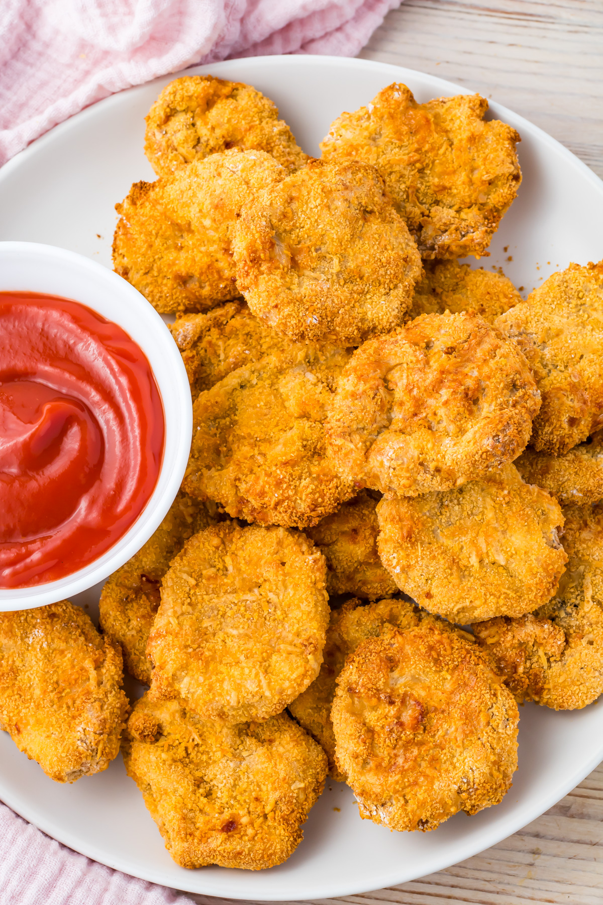 A plate of crispy, air fryer homemade chicken nuggets is served with a small dish of ketchup on the side.