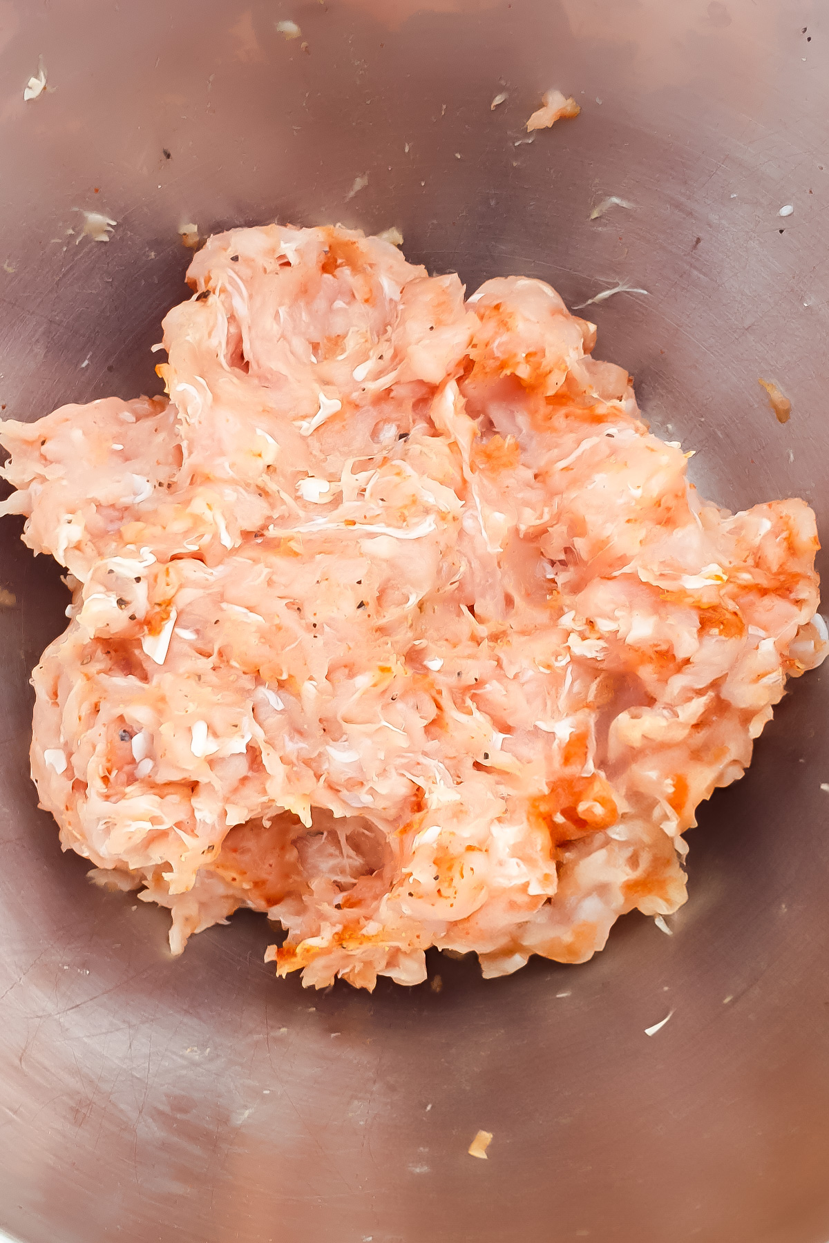 Raw ground chicken mixed with seasonings in a stainless steel bowl.