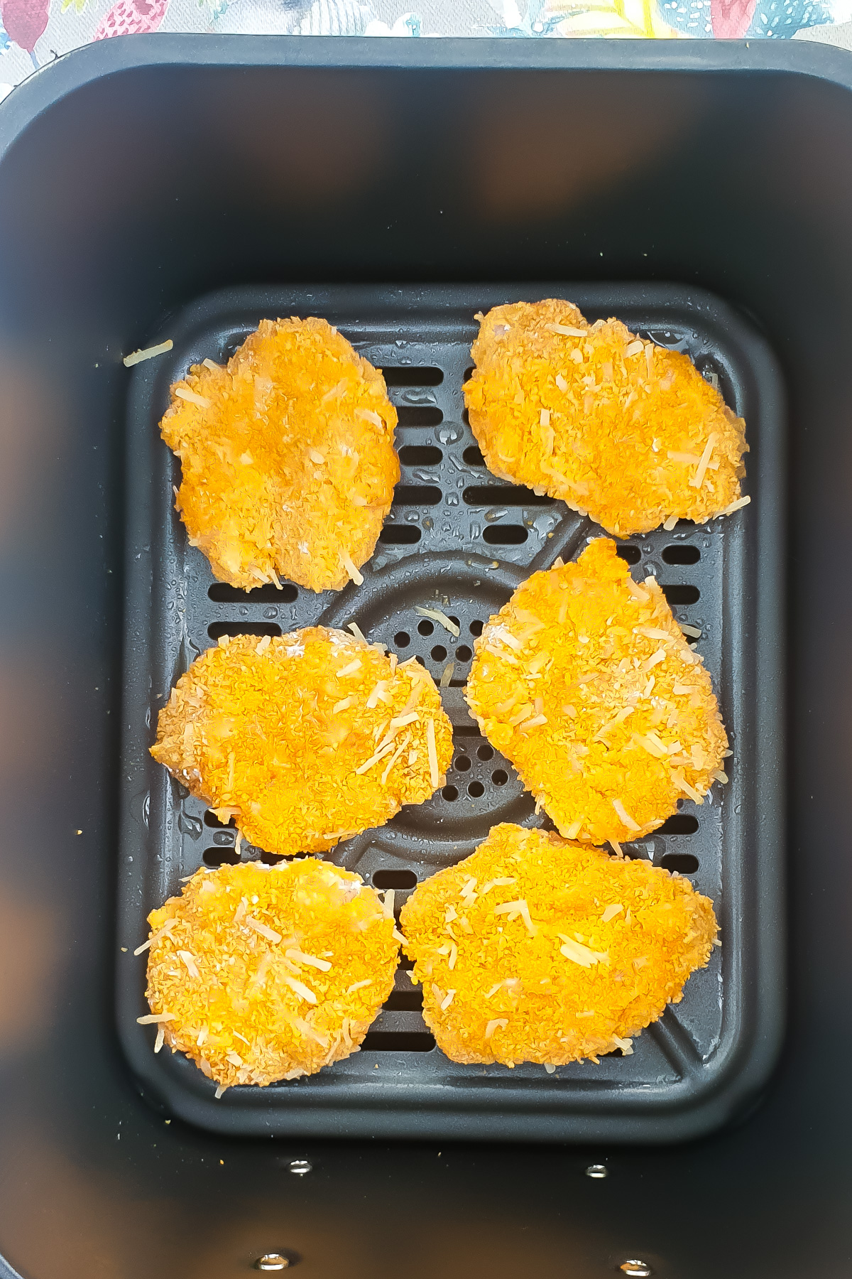 Six breaded homemade chicken nuggets are arranged in a single layer inside the basket of an air fryer.