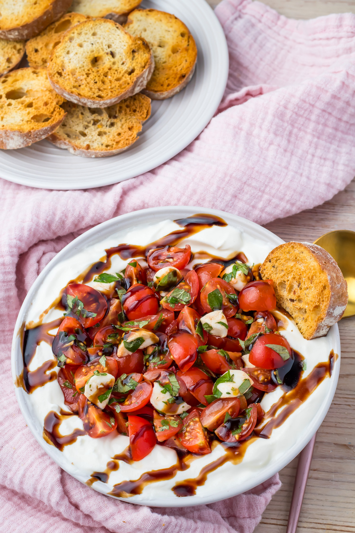 A plate of whipped cottage cheese topped with chopped tomatoes, basil, and balsamic glaze makes a flavorful Bruschetta Dip appetizer, served with toasted bread slices on a nearby plate.