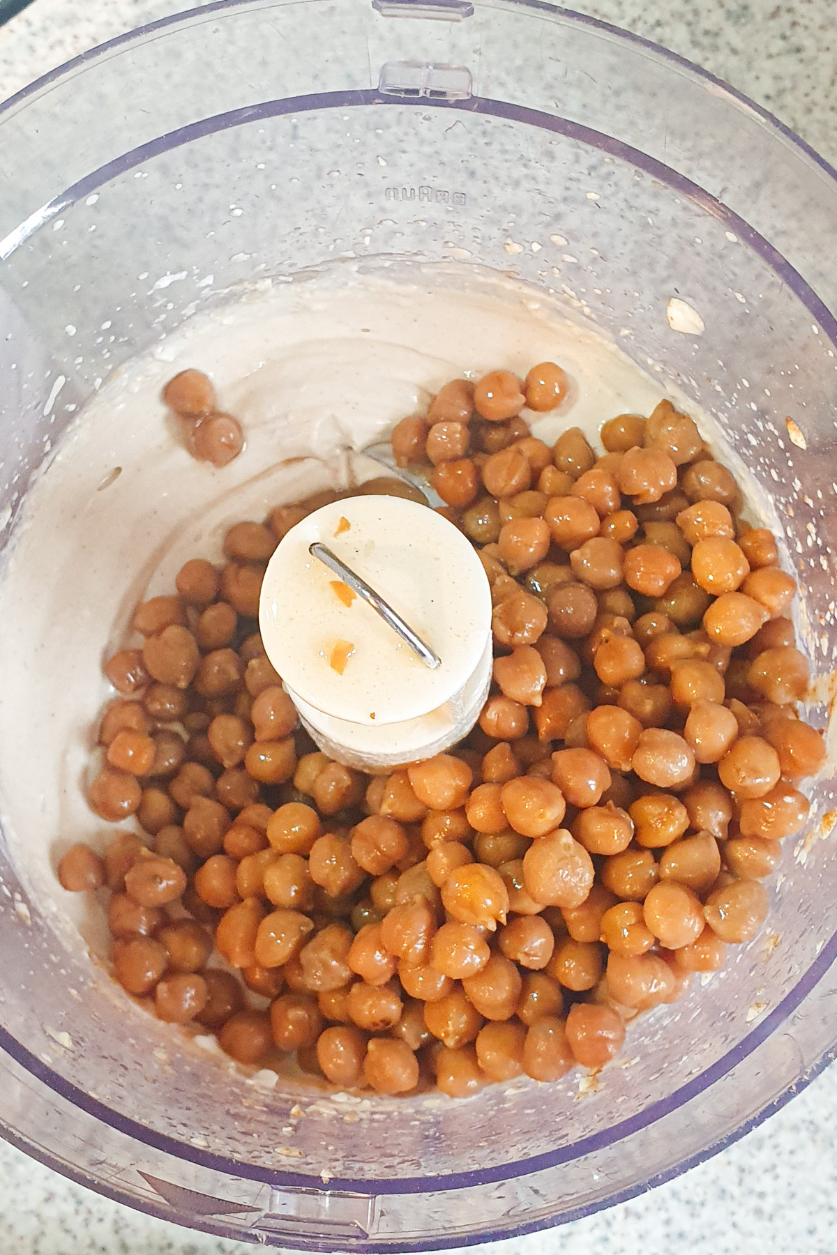 Chickpeas in a food processor bowl with some residual mixture underneath and on the sides.