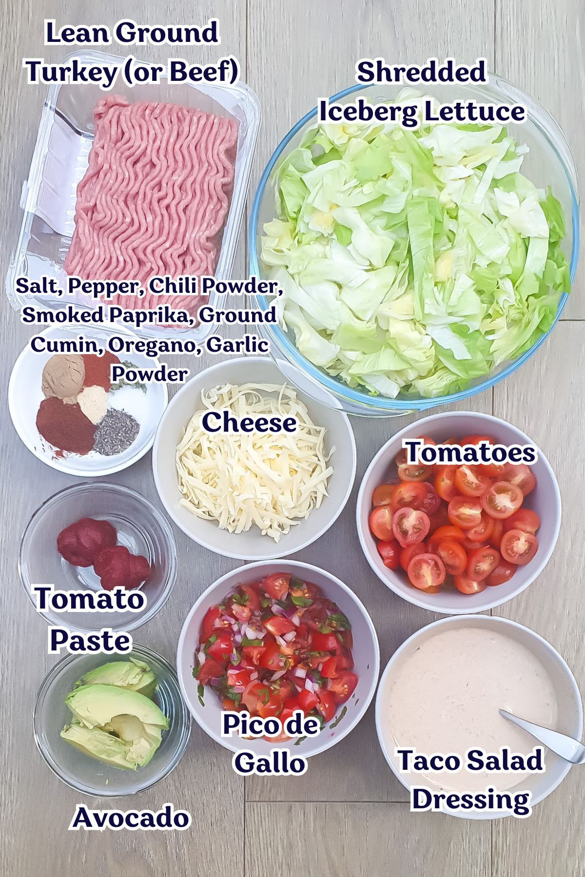 A flat lay of Healthy Taco Salad ingredients: ground meat, shredded lettuce, cheese, tomatoes, avocado, tomato paste, pico de gallo, salad dressing, and various spices.