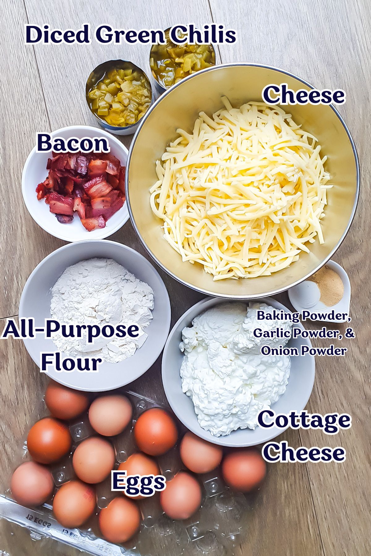 Various ingredients for a cottage cheese casserole are arranged on a wooden surface, including eggs, cottage cheese, shredded cheese, diced green chilis, bacon, flour, and small bowls of powders.