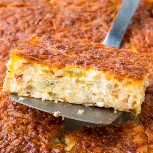 A close-up of a spatula lifting a square slice of cottage cheese egg casserole with a golden, crispy top and a soft, cheesy interior.