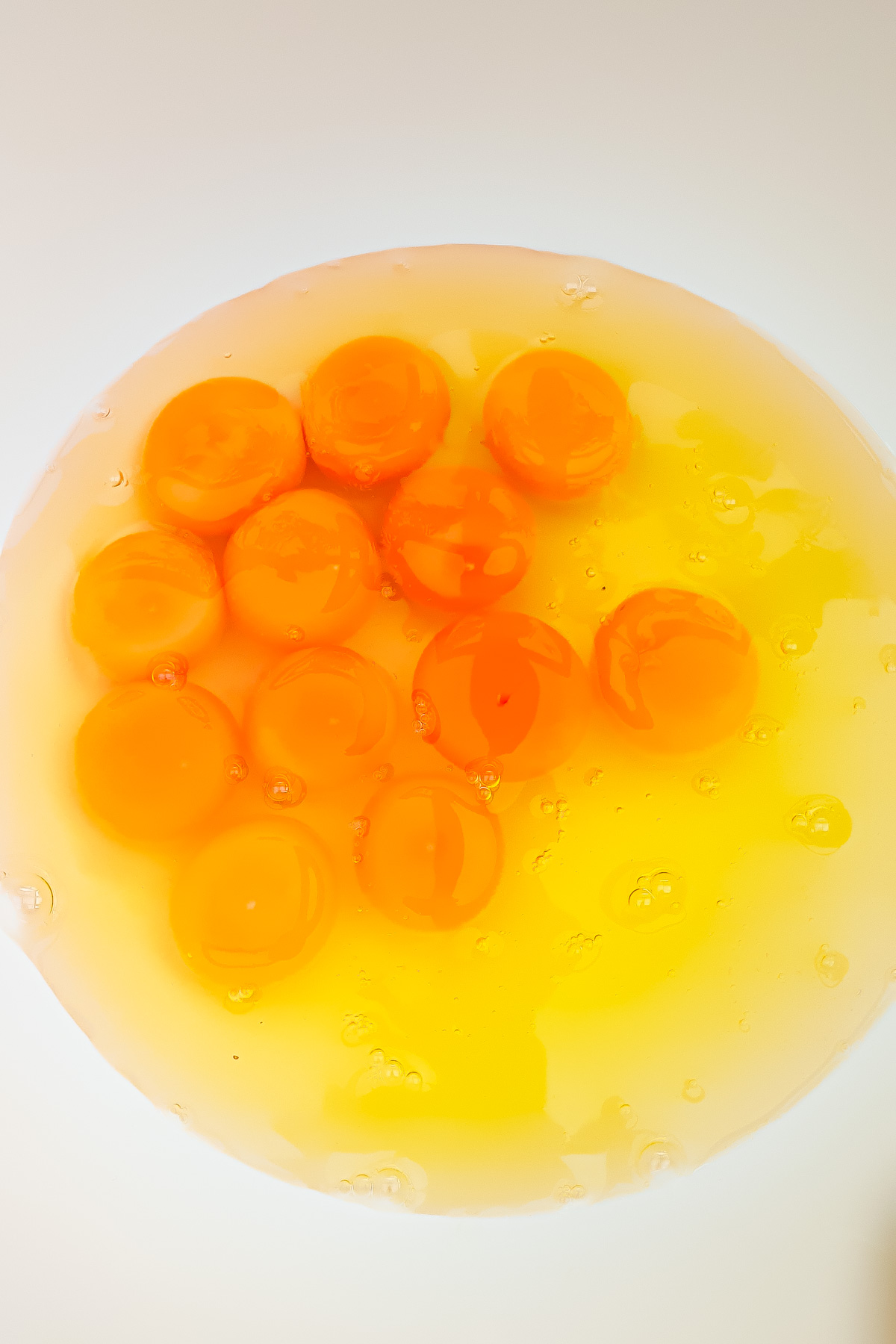 A close-up view of twelve raw egg yolks and whites in a white bowl.