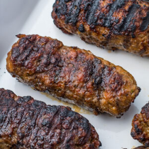 Three grilled lamb Koftas with char marks are placed on a white surface.