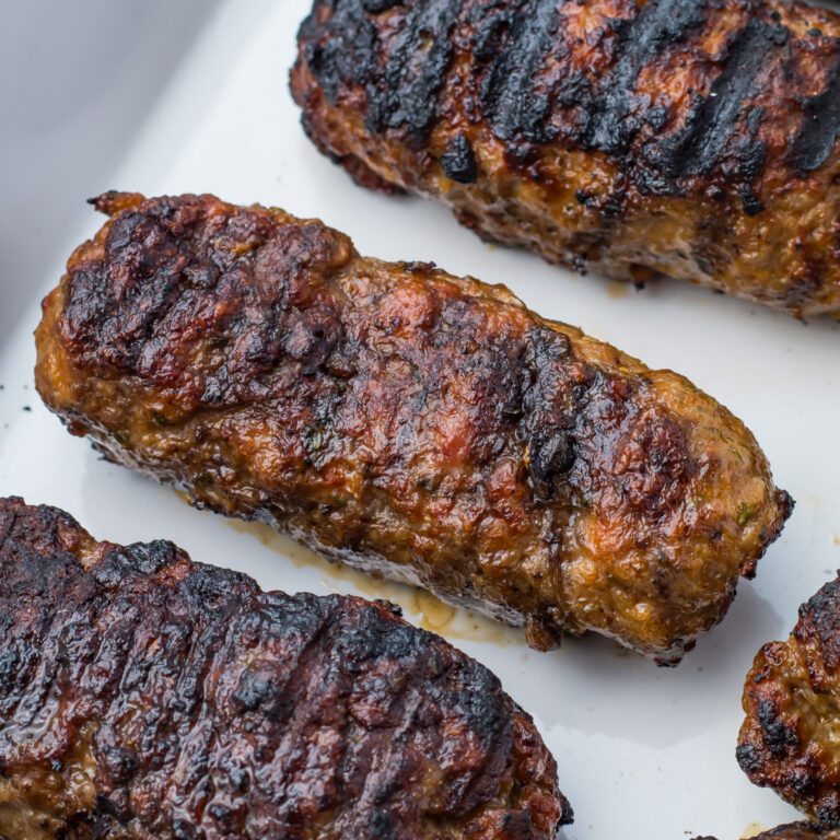 Three grilled lamb Koftas with char marks are placed on a white surface.