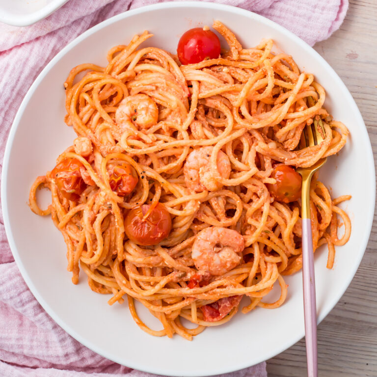 A plate of shrimp pasta bake with cherry tomatoes in a rich red sauce, served with a fork on the side.