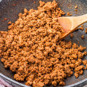 Cooked and seasoned taco meat in a skillet, being stirred with a wooden spoon.