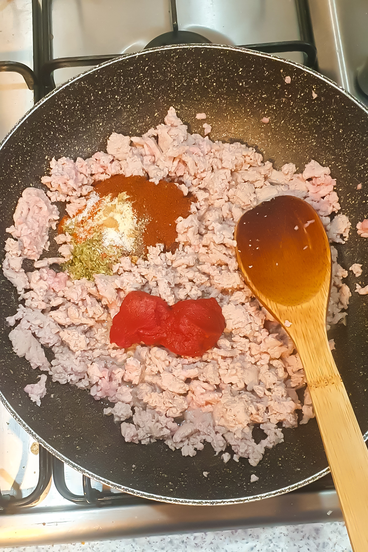 Ground meat simmers in a frying pan with tomato paste and spices, being stirred with a wooden spoon—perfect for any taco meat recipe.