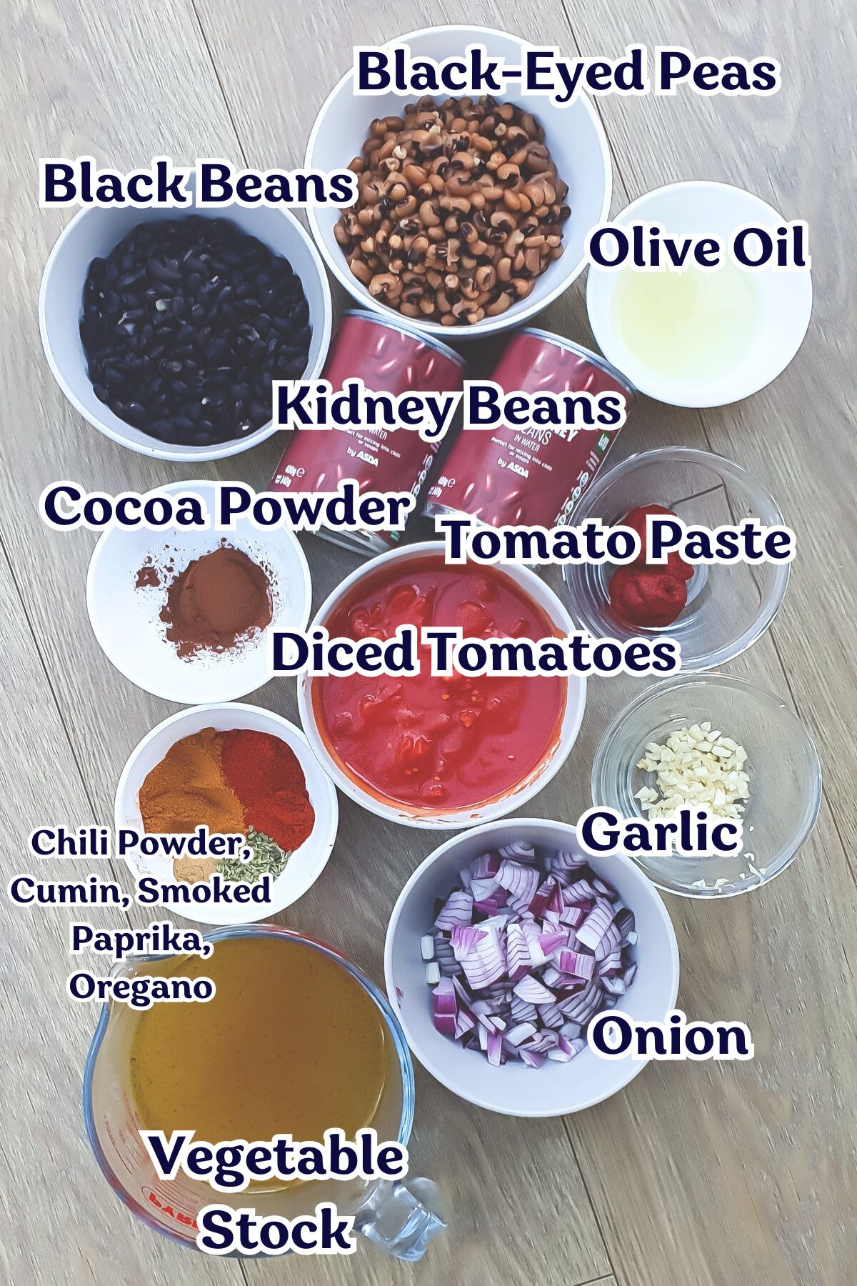 Assorted ingredients for high protein vegan chili, including black beans, black-eyed peas, kidney beans, olive oil, cocoa powder, tomato paste, diced tomatoes, spices, garlic, onion, and vegetable stock.