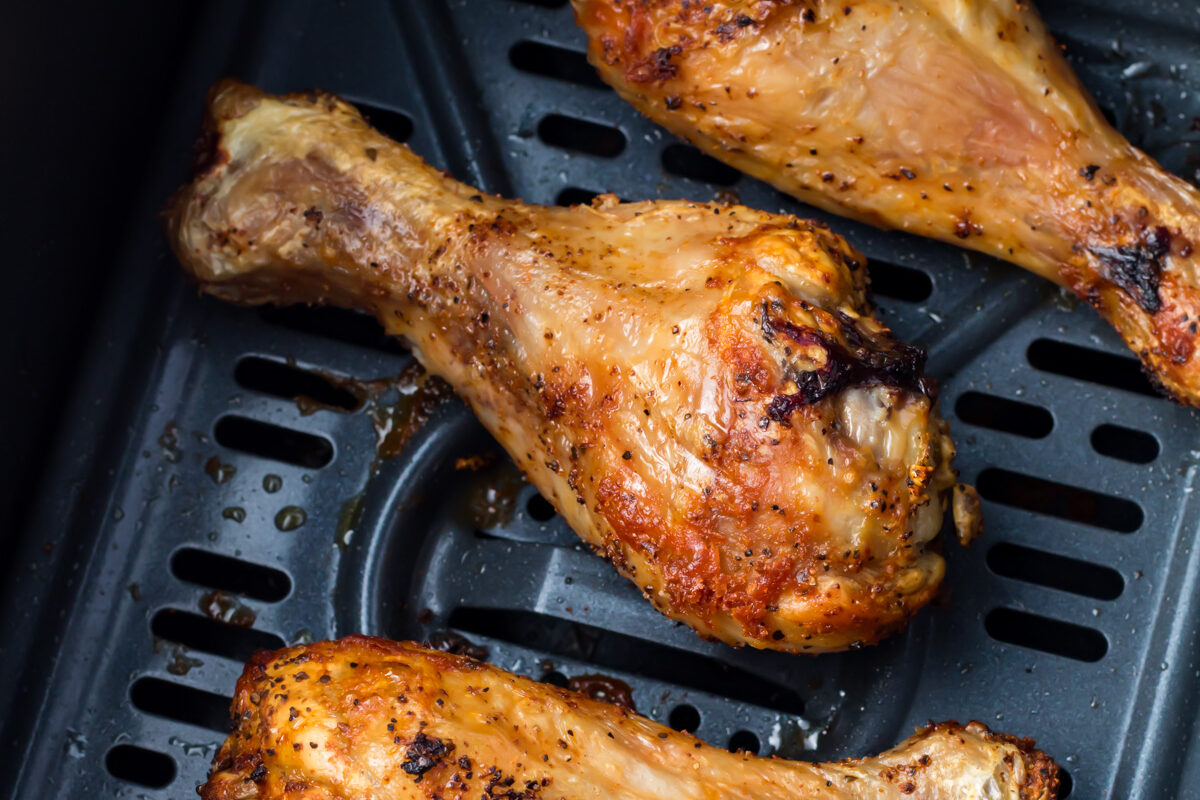 Four perfectly cooked air fryer chicken legs in an air fryer basket.