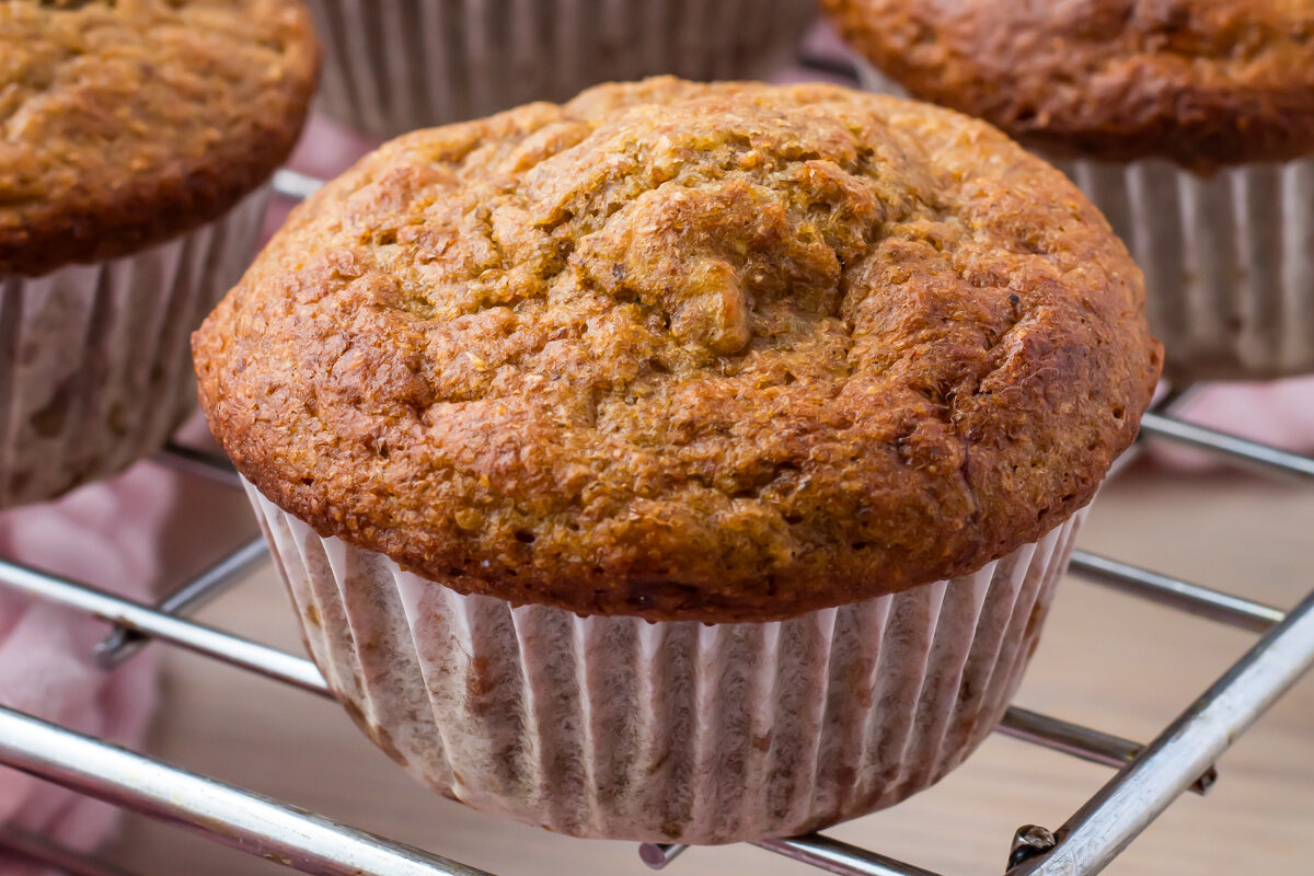 Close-up of freshly baked banana muffins cooling on a wire rack, with a pink cloth underneath.