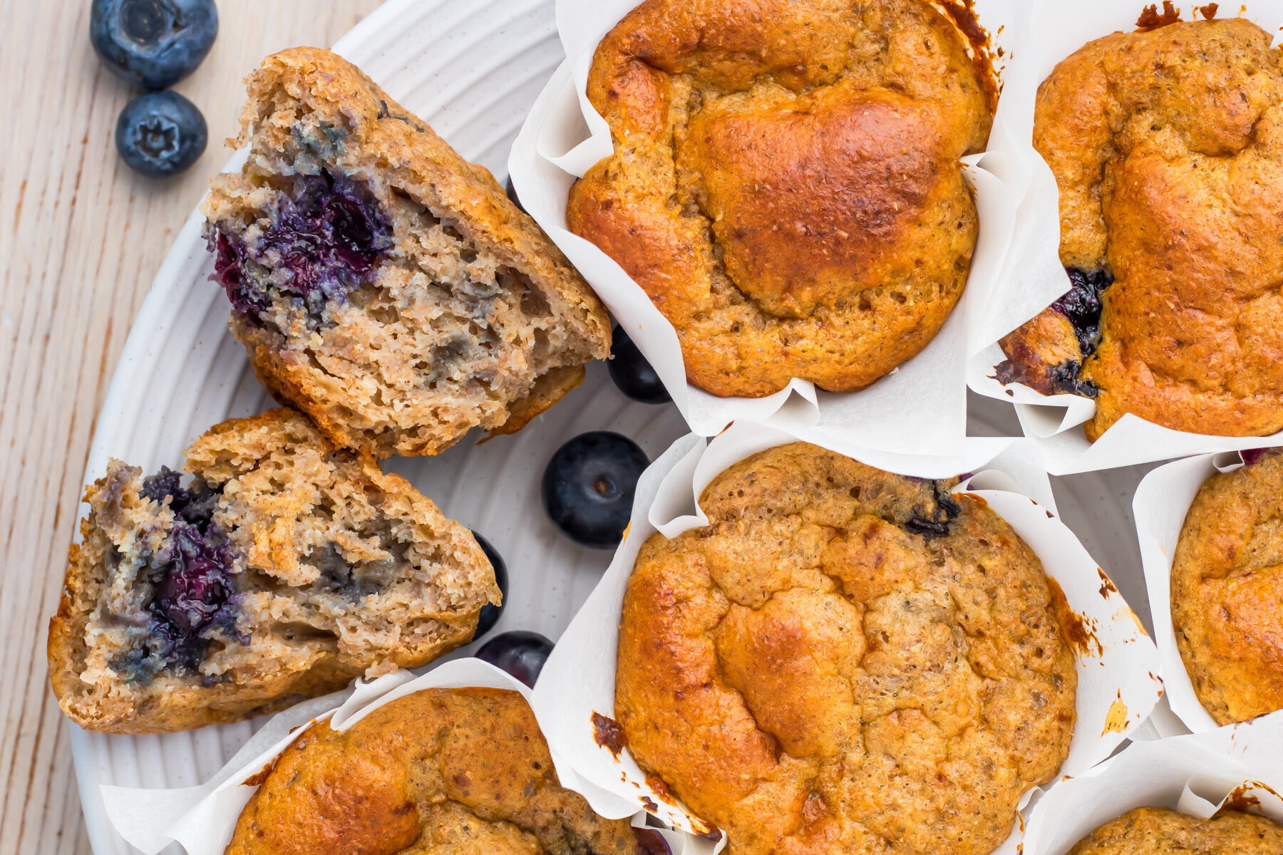 A plate of cottage cheese blueberry muffins, some whole and one cut in half to reveal the cottage cheese and blueberry filling, with a few blueberries scattered nearby.