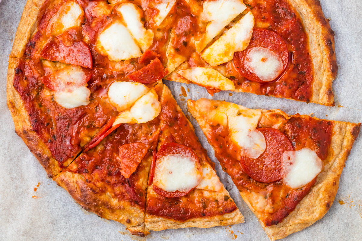 A cottage cheese pizza with melted cheese cut into slices and placed on parchment paper.