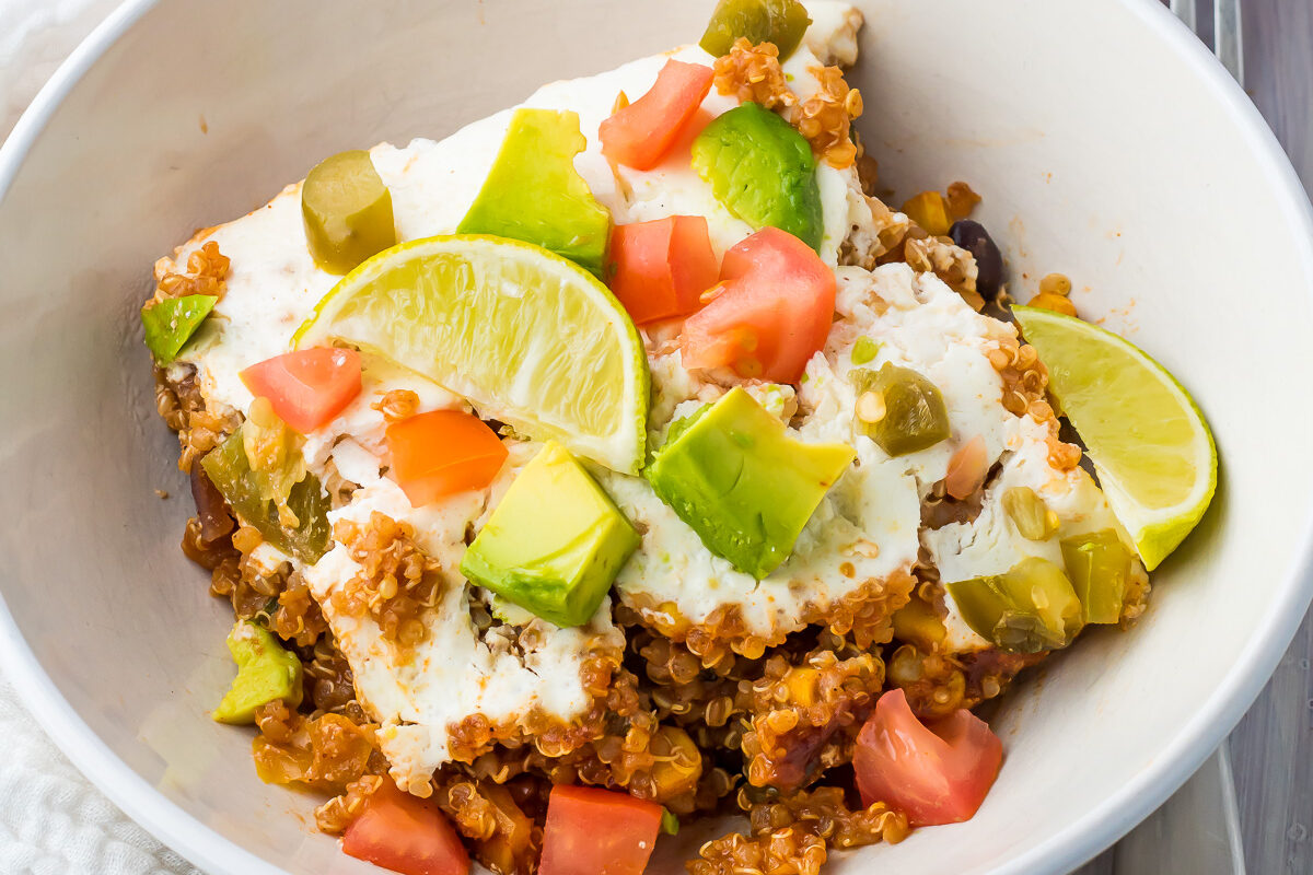 Quinoa Enchilada Casserole in a white bowl with a large red casserole dish in the background.