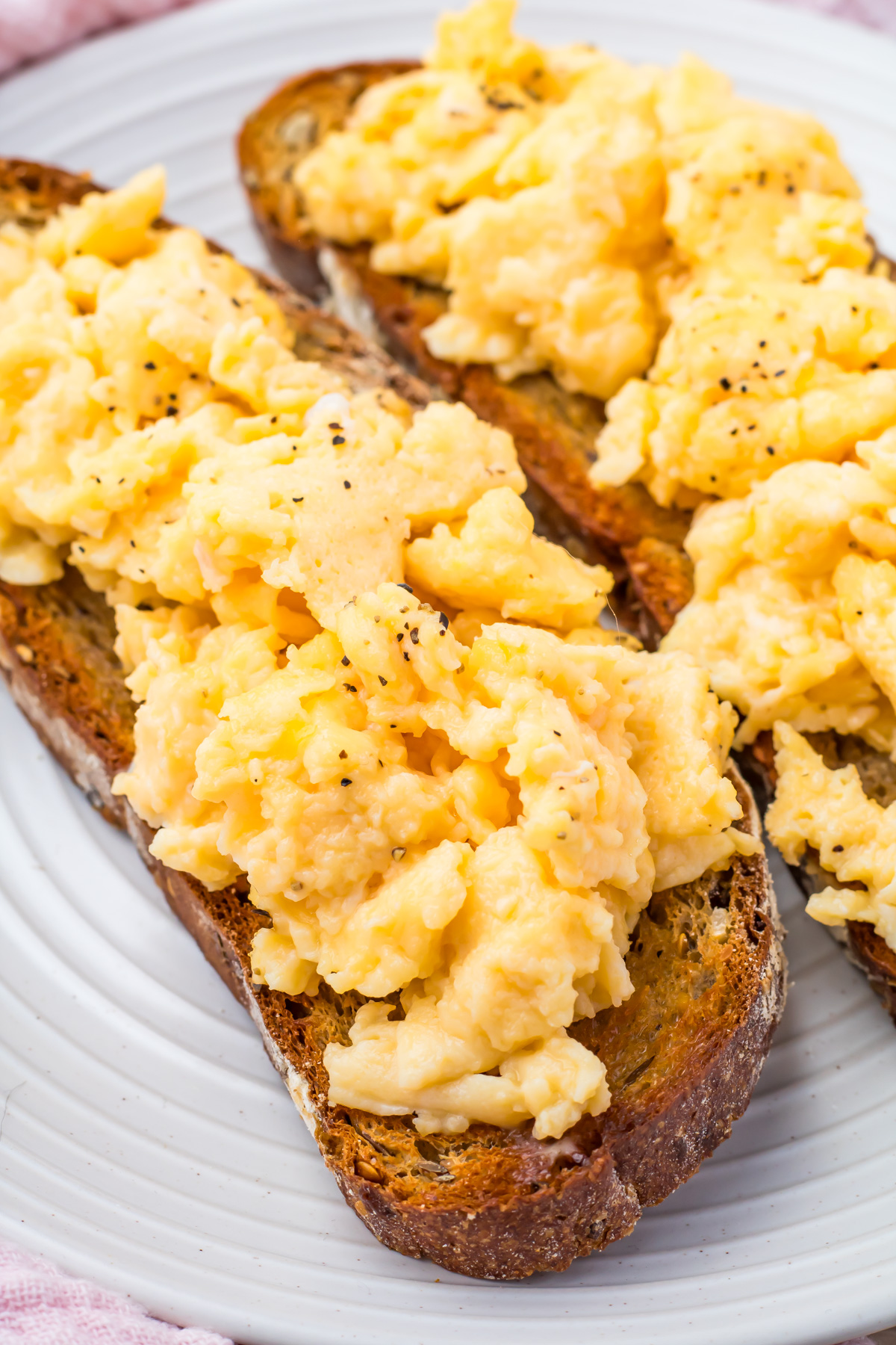 Two slices of toasted bread topped with scrambled eggs with water are served on a white plate.