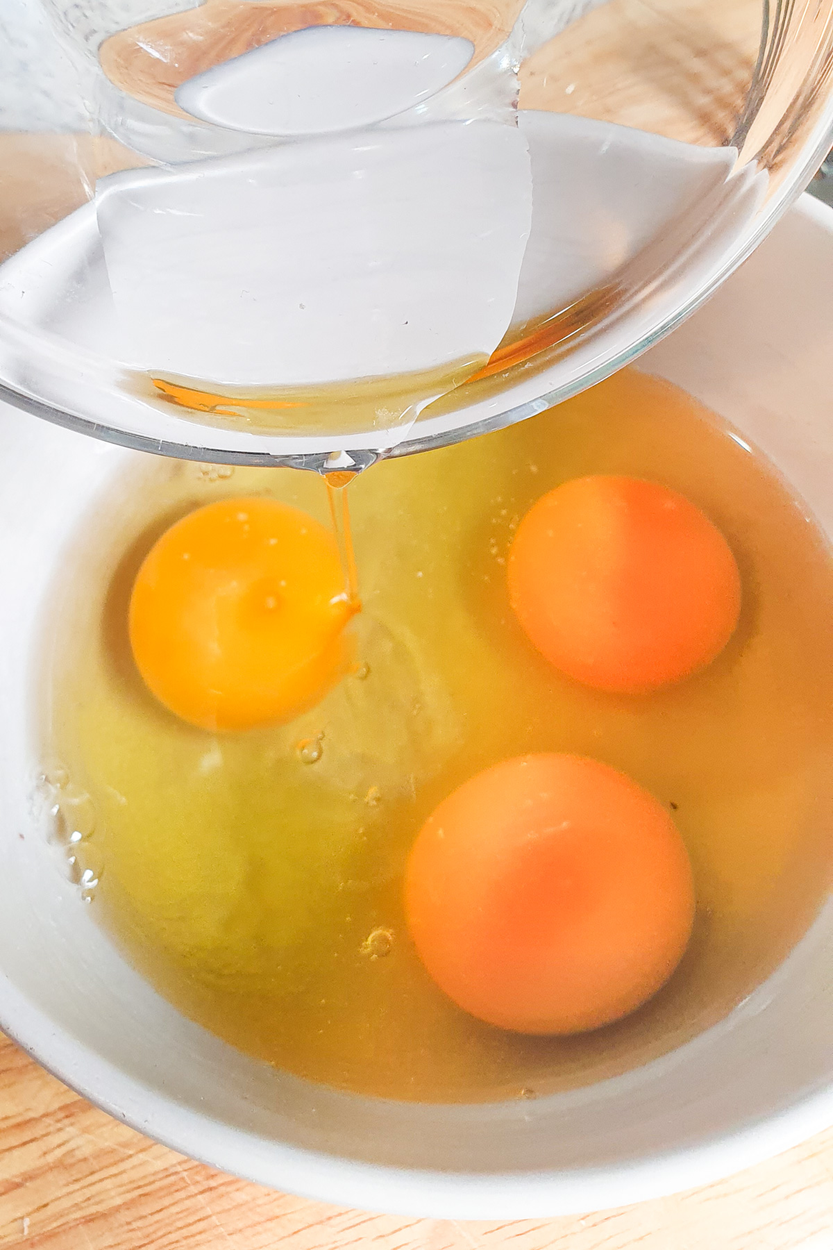 A clear bowl pours a raw egg into a white bowl containing two already cracked eggs.