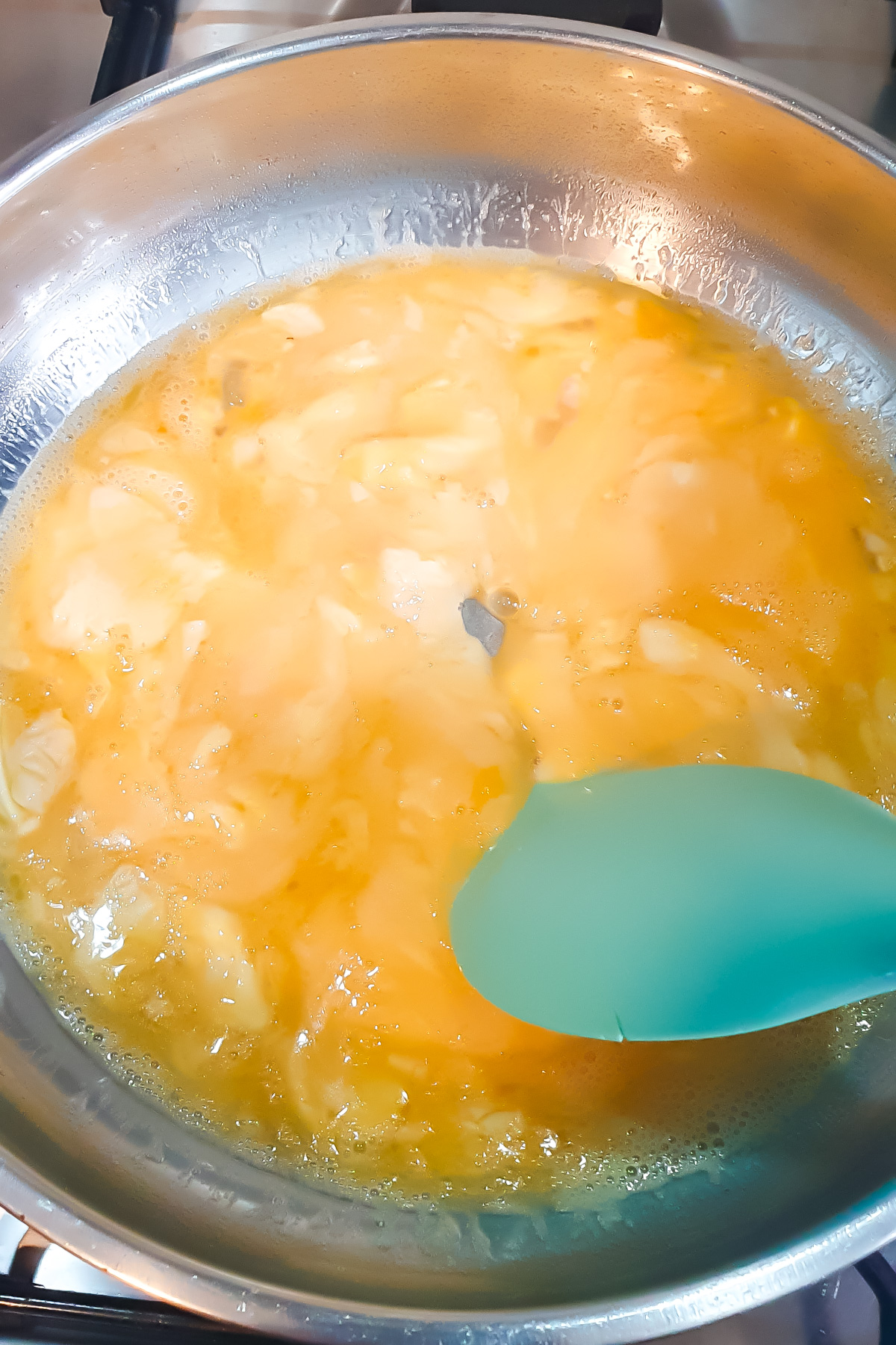 Eggs being scrambled in a stainless steel pan with a green spatula on a stove.