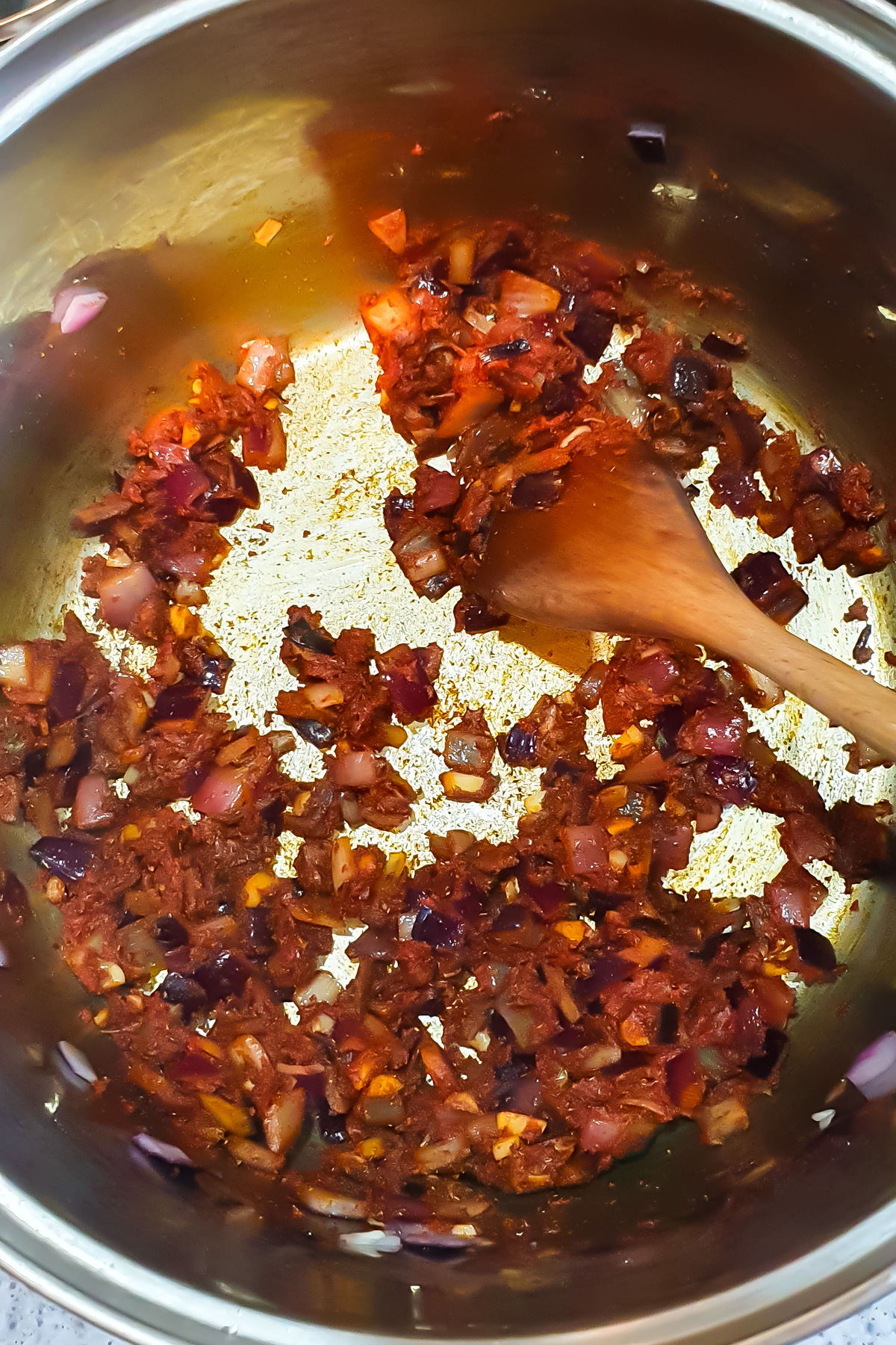 Diced onions and tomatoes sautéing in a stainless steel pot, stirred with a wooden spoon—the perfect base for a high protein Vegan Chili.