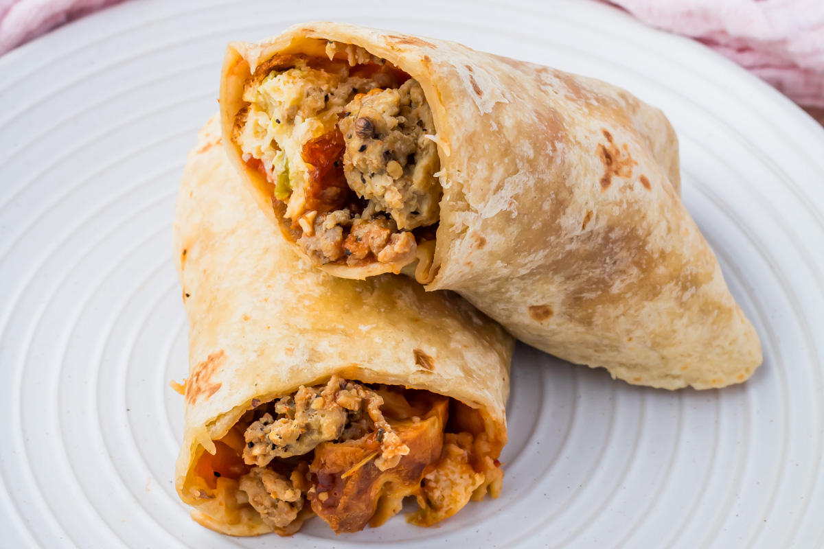Two high-protein breakfast burritos filled with scrambled eggs, ground meat, and vegetables on a white plate&mdash;a perfect recipe to start your day.
