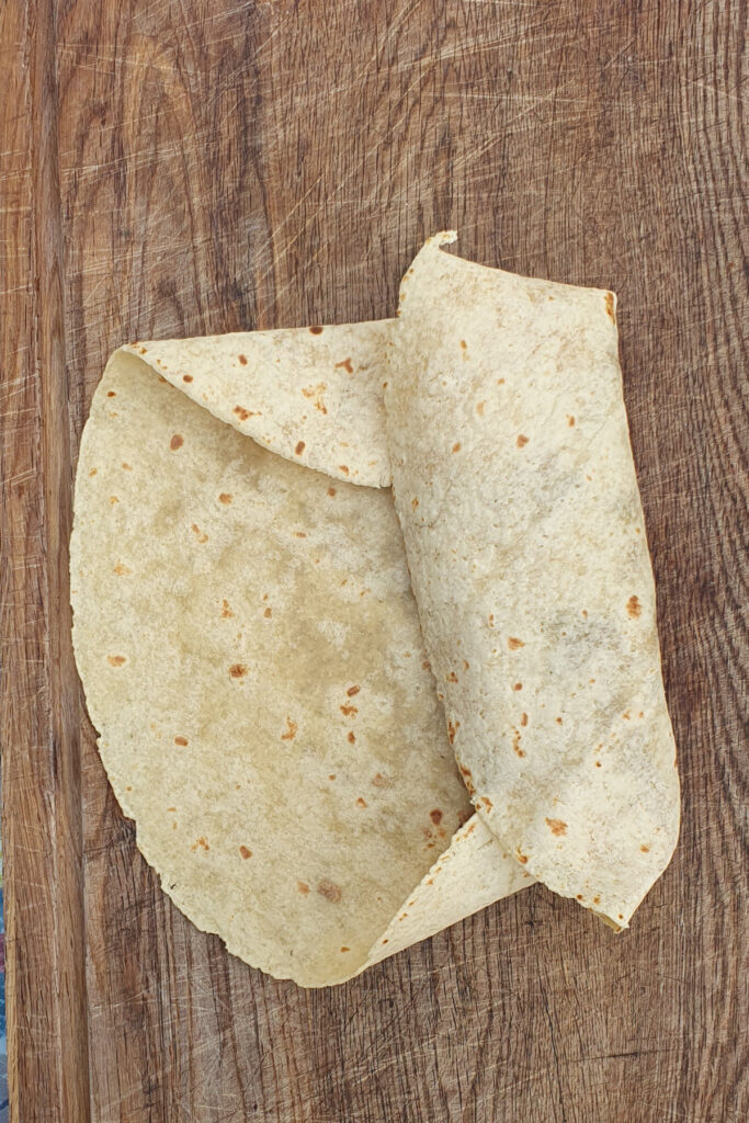 Two flour tortillas, perfect for crafting a high protein breakfast burrito, partially overlap on a wooden cutting board.