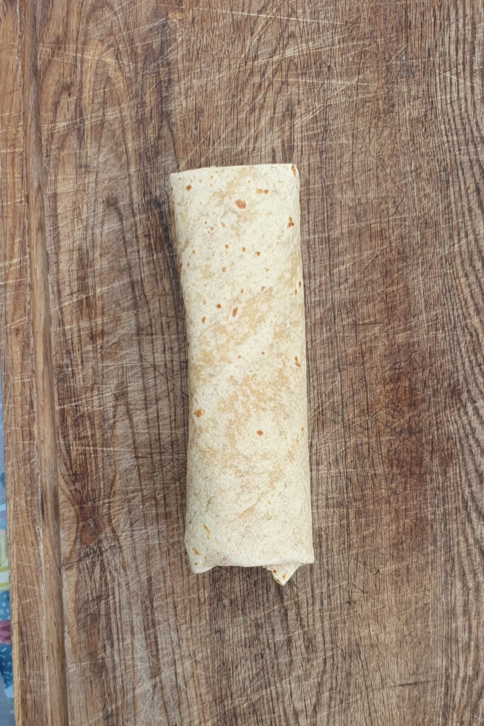 A single high protein breakfast burrito sits rolled on a wooden surface.
