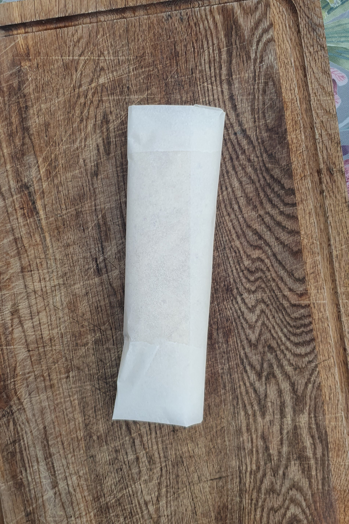 A high protein breakfast burrito wrapped in white parchment paper rests on a wooden cutting board.