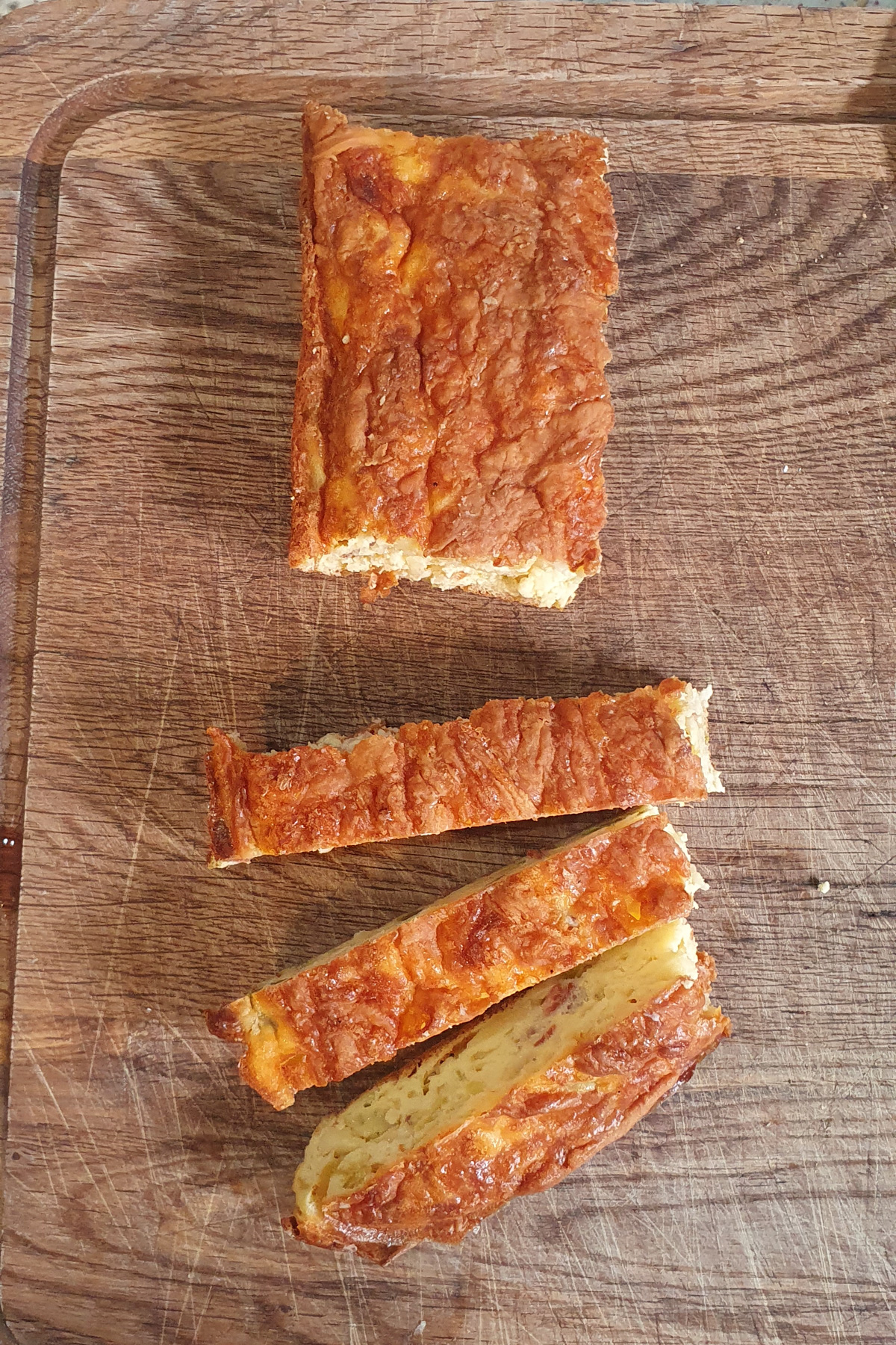 A loaf of cheesy egg casserole on a wooden cutting board, with one large piece and two sliced pieces visible.