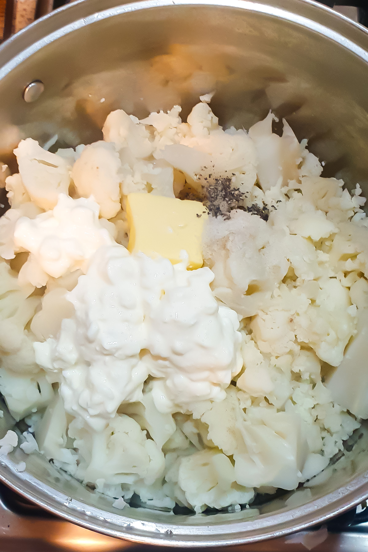 A pot filled with cooked cauliflower florets, cottage cheese, butter, and black pepper sits ready to be mixed together.
