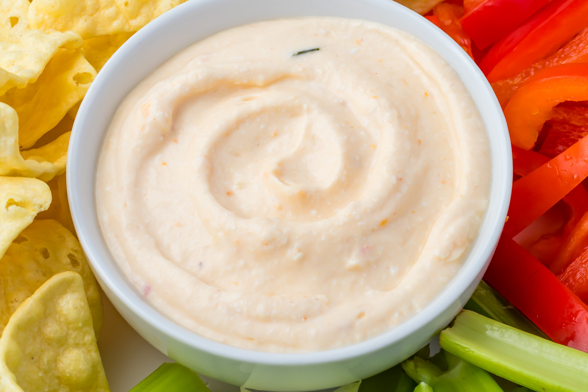 A bowl of creamy cottage cheese queso dip surrounded by tortilla chips, celery sticks, and sliced red bell peppers.