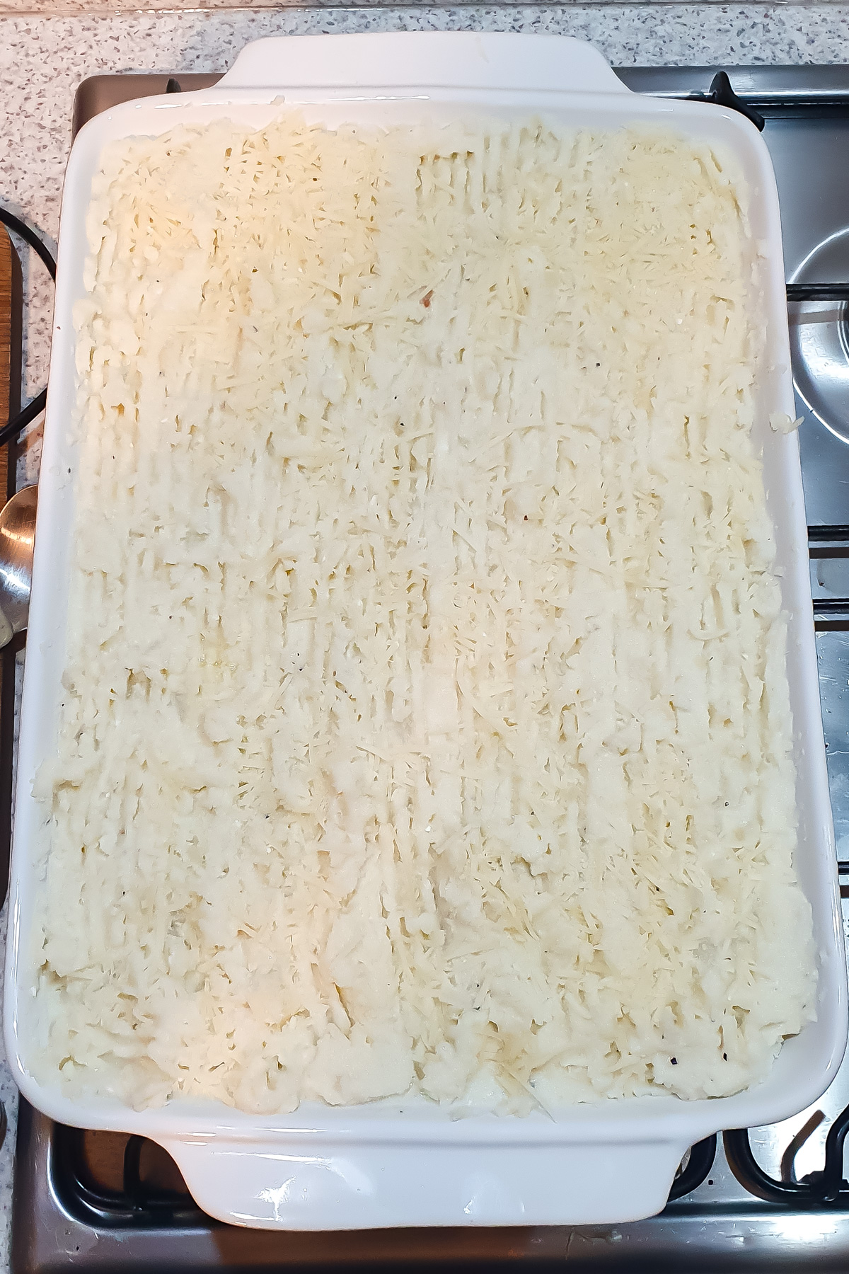 A rectangular white baking dish filled with an even layer of mashed cauliflower.