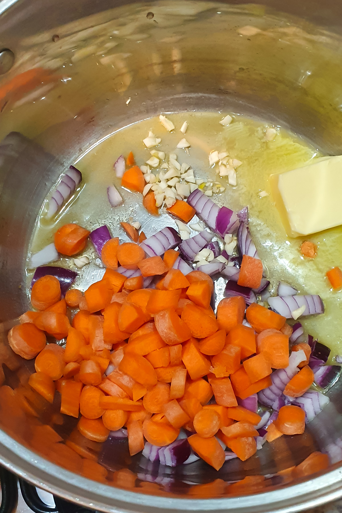 Chopped carrots, red onions, and garlic in a pot with butter, beginning to sauté.
