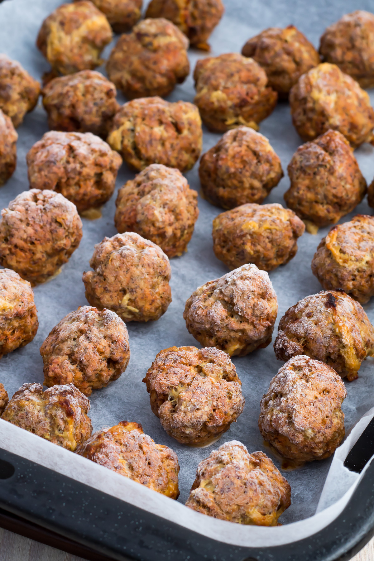 A baking tray lined with parchment paper holds several evenly spaced, Frozen meatballs that are browned and slightly crisp on the outside.