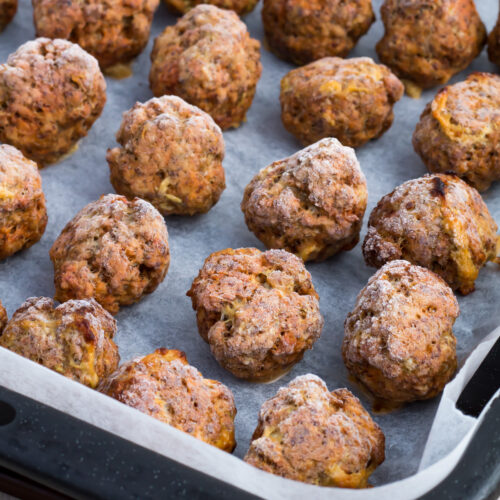 A baking tray lined with parchment paper holds several evenly spaced, frozen meatballs with a browned, slightly crispy exterior.