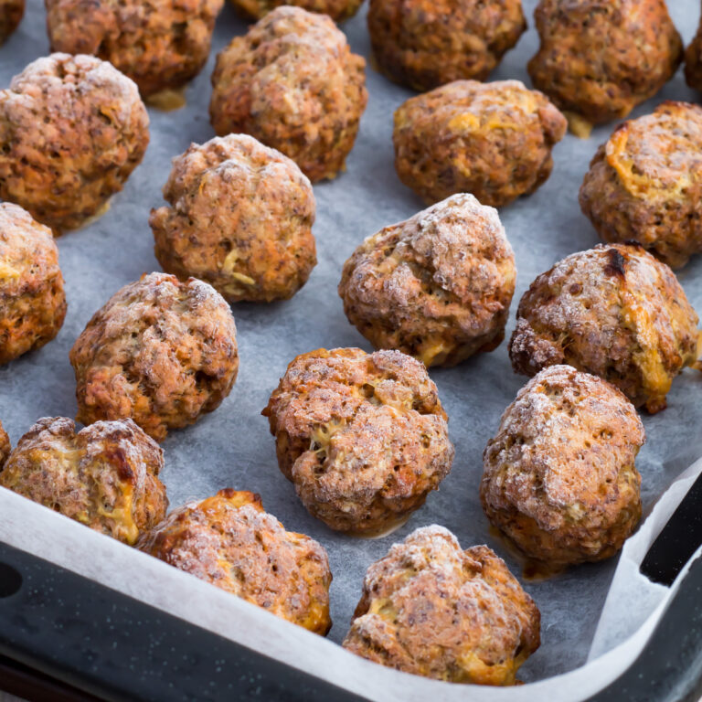 A baking tray lined with parchment paper holds several evenly spaced, frozen meatballs with a browned, slightly crispy exterior.