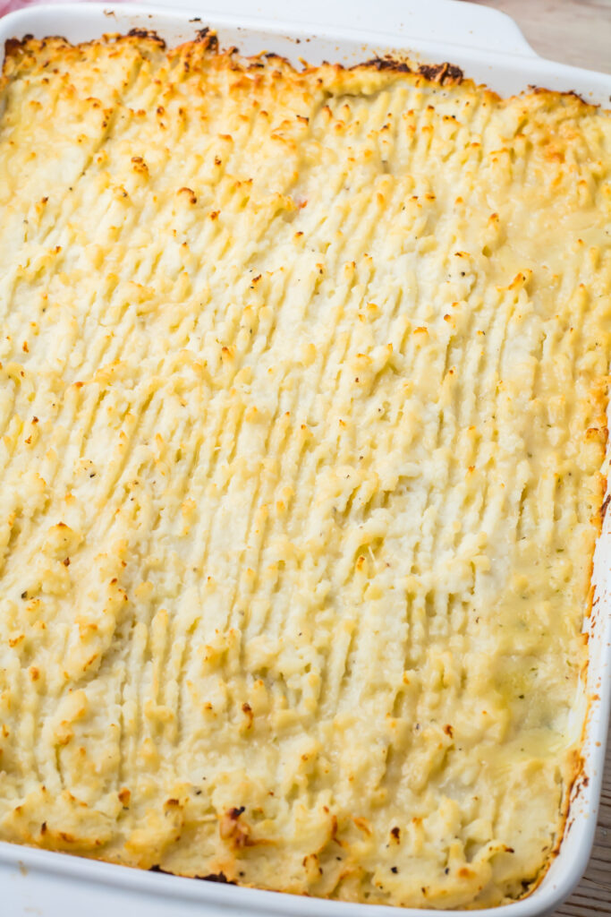 A baked fish pie in a white dish, topped with mashed cauliflower that has a ridged texture and lightly golden edges.