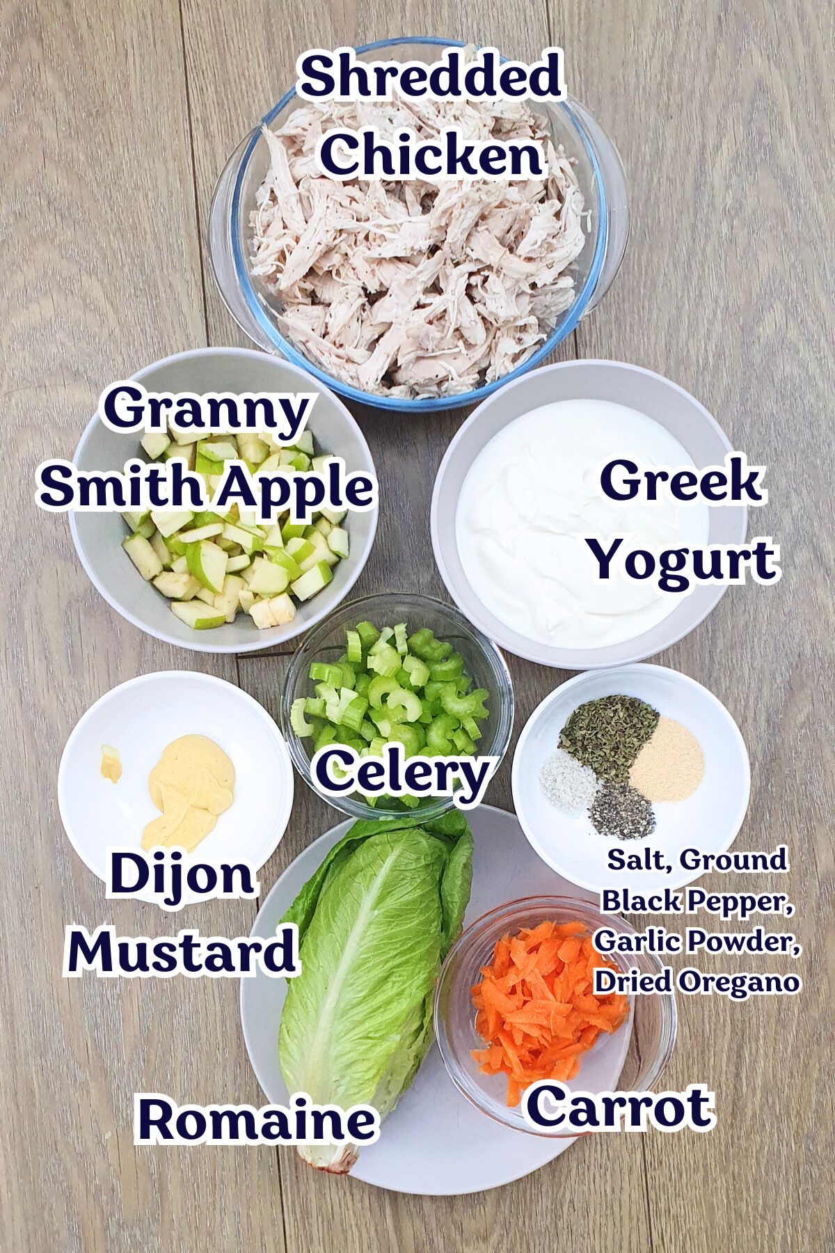 Bowls filled with Greek yogurt, Granny Smith apple, celery, carrot, Dijon mustard, and romaine lettuce are arranged on a wooden surface.