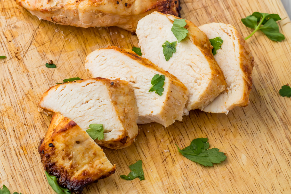 Sliced cooked air fryer frozen chicken breast on a wooden cutting board, garnished with fresh parsley leaves.