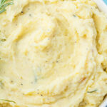 A bowl of creamy cottage cheese mashed potatoes, garnished with a sprig of rosemary.