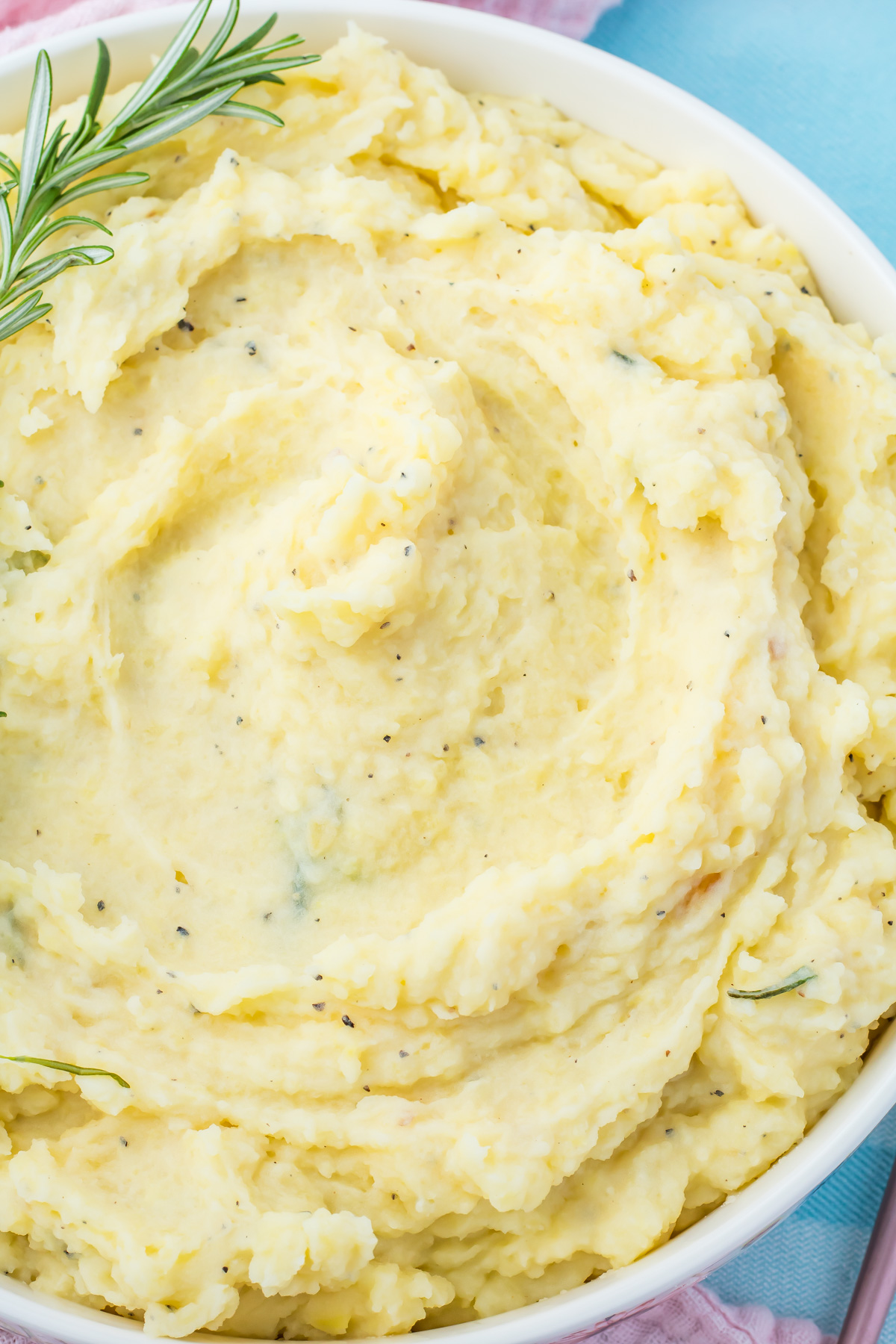 A bowl of creamy cottage cheese mashed potatoes, garnished with a sprig of rosemary.