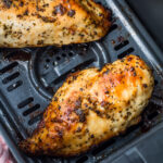 Two cooked, seasoned air fryer boneless chicken breasts in a basket, showing a golden brown, slightly charred surface.