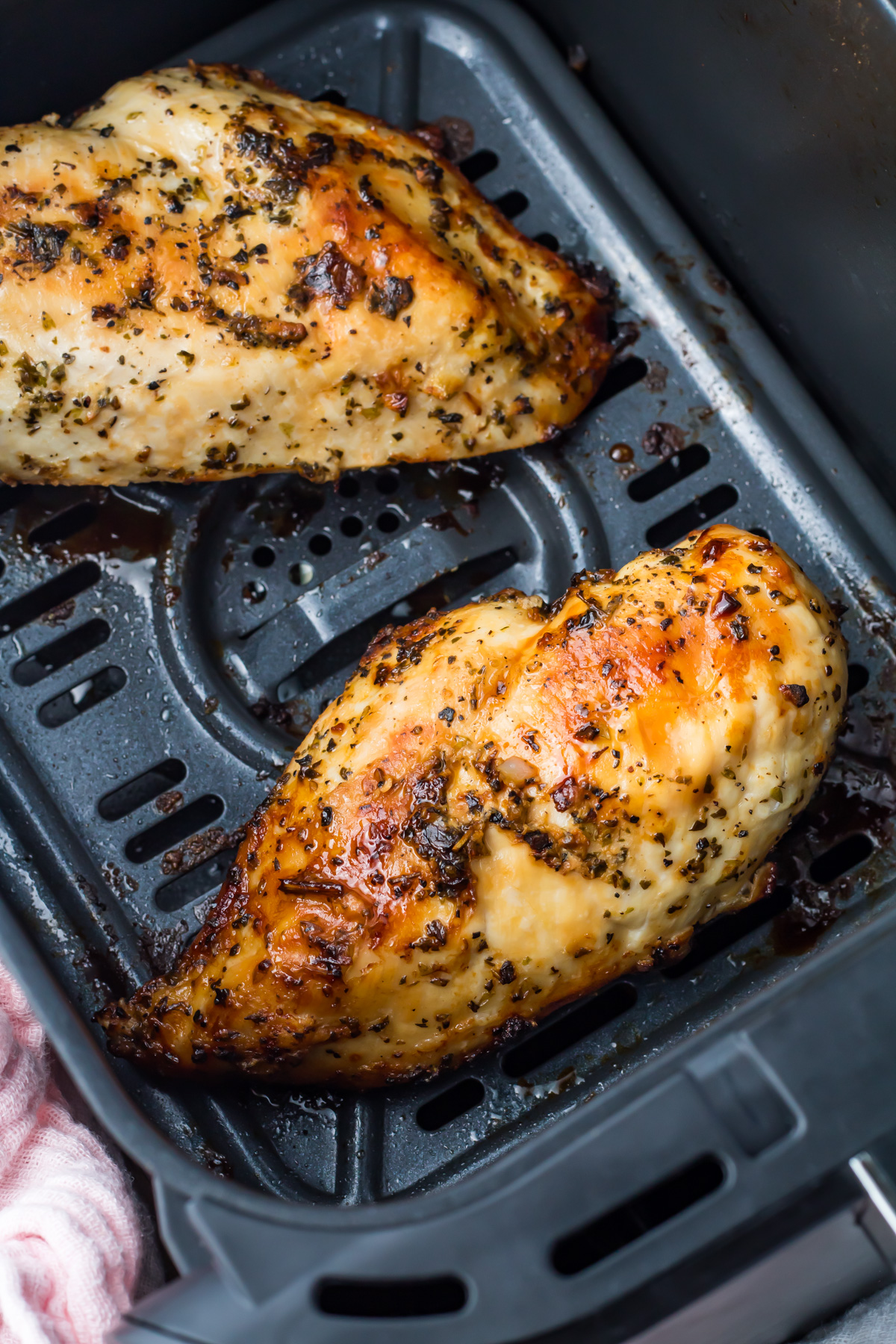 Two cooked, seasoned air fryer boneless chicken breasts in a basket, showing a golden brown, slightly charred surface.