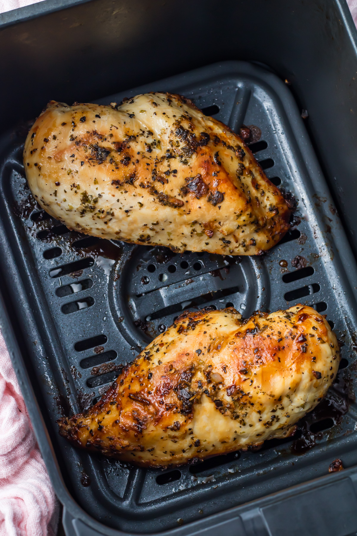 Two seasoned, cooked skinless boneless chicken breasts sit in the basket of an air fryer, making for a perfect air fryer chicken breast meal.