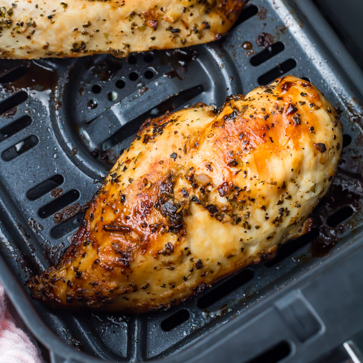 A boneless skinless chicken breast, perfectly seasoned, sits in the basket of an air fryer.