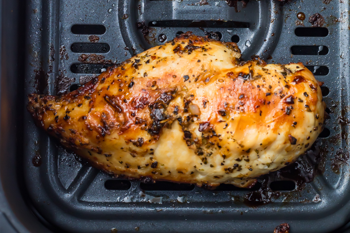 A cooked, seasoned air fryer chicken breast sits in the basket, showing a browned and slightly crispy surface.