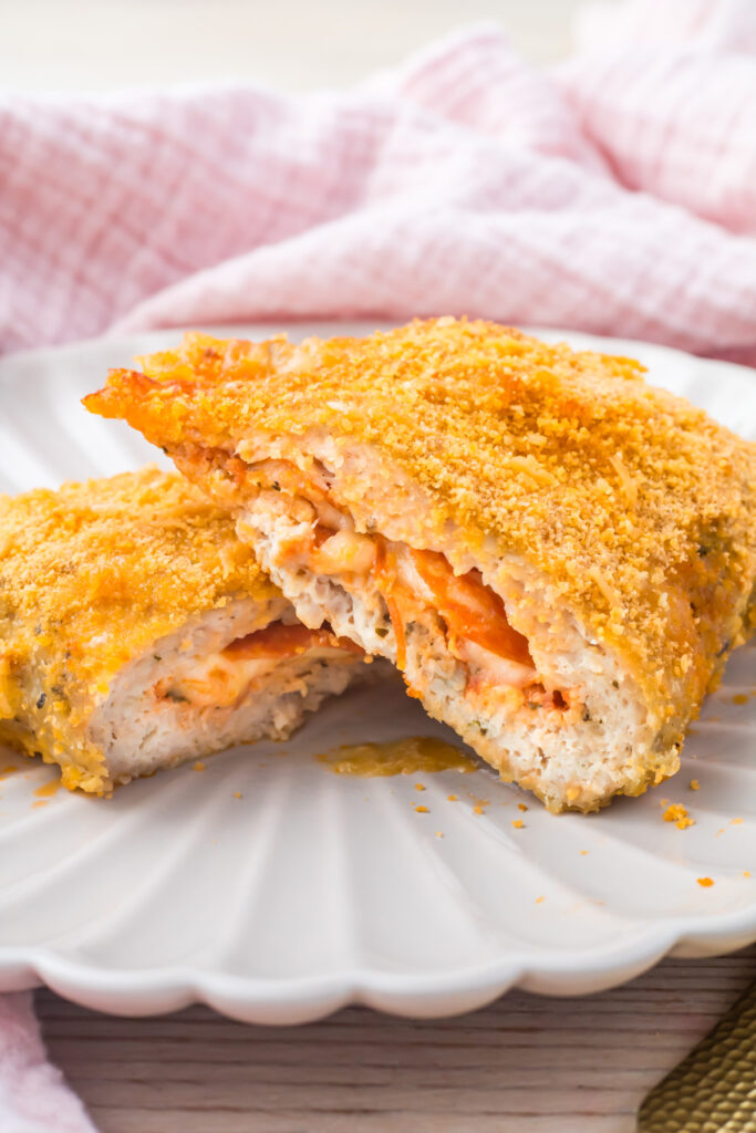 High protein pizza pocket stuffed with cheese and pepperoni, sliced open on a white plate with a pink cloth in the background.