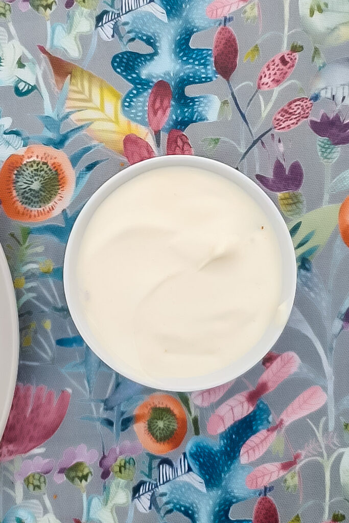 A white bowl filled with creamy greek yogurt protein cheesecake sits on a colorful floral-patterned tablecloth.