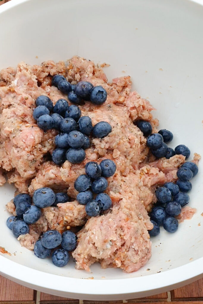 Ground meat mixture and fresh blueberries in a large white mixing bowl.